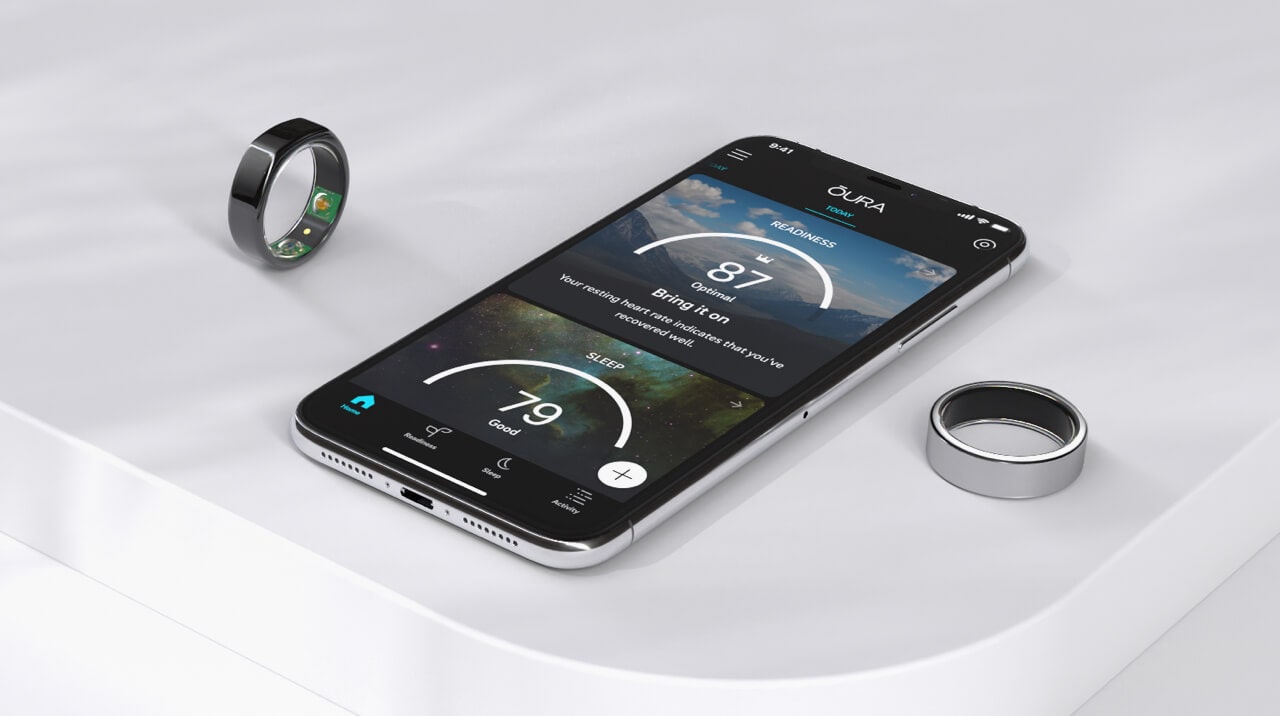 A table with a couple of Oura rings and a mobile phone displaying the Oura app.