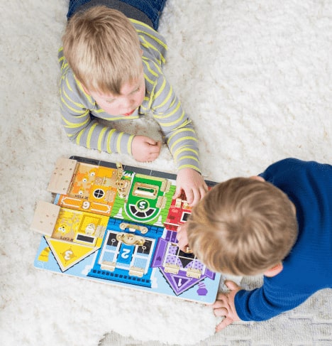 Two little boys laying on the floor playing with a puzzle.