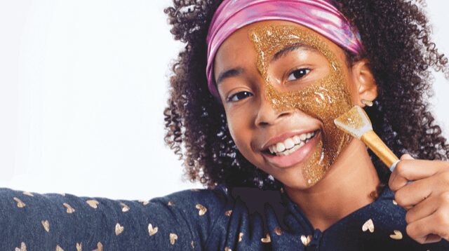 A girl putting on a gold glitter face mask.