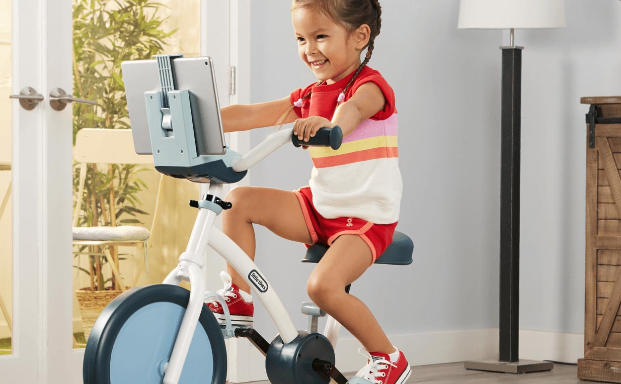 A young girl riding a Little Tikes Pelican stationary bike.