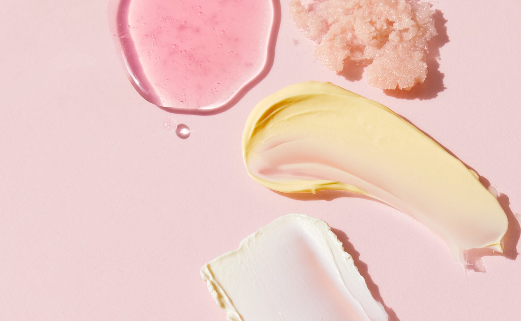 A pink background with different serums/lotions spread across.