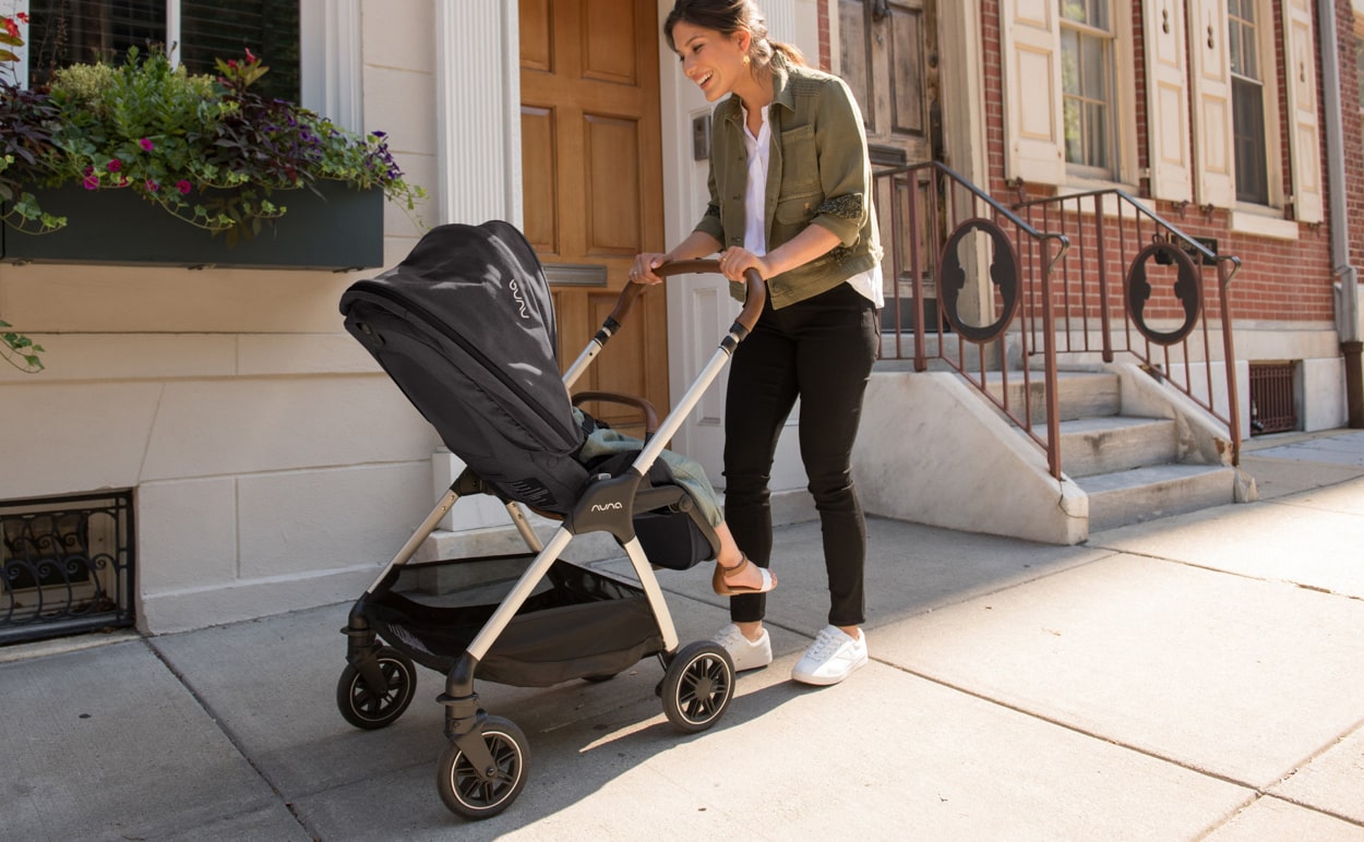 A mother walking down a sidewalk while pushing a baby stroller.