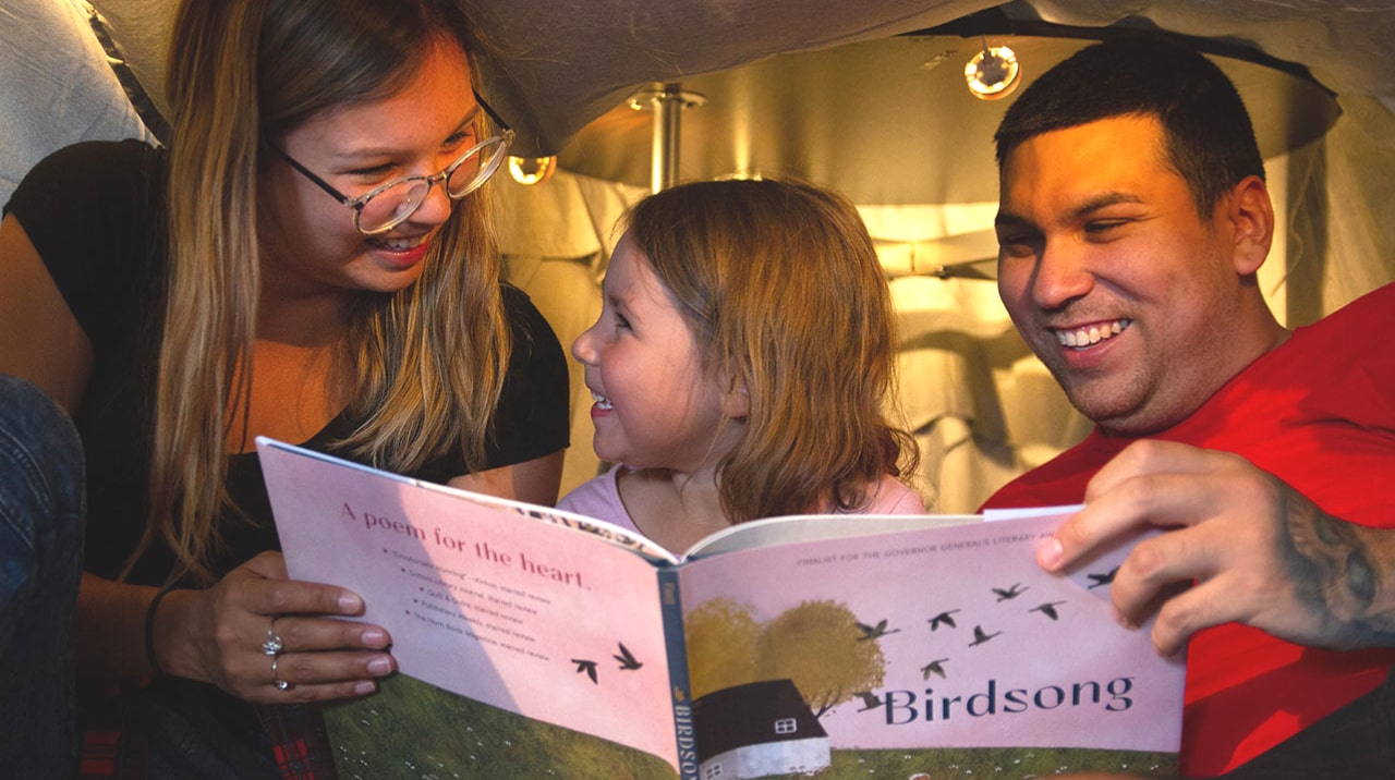 Two parents reading the book "Birdsong" to their daughter.