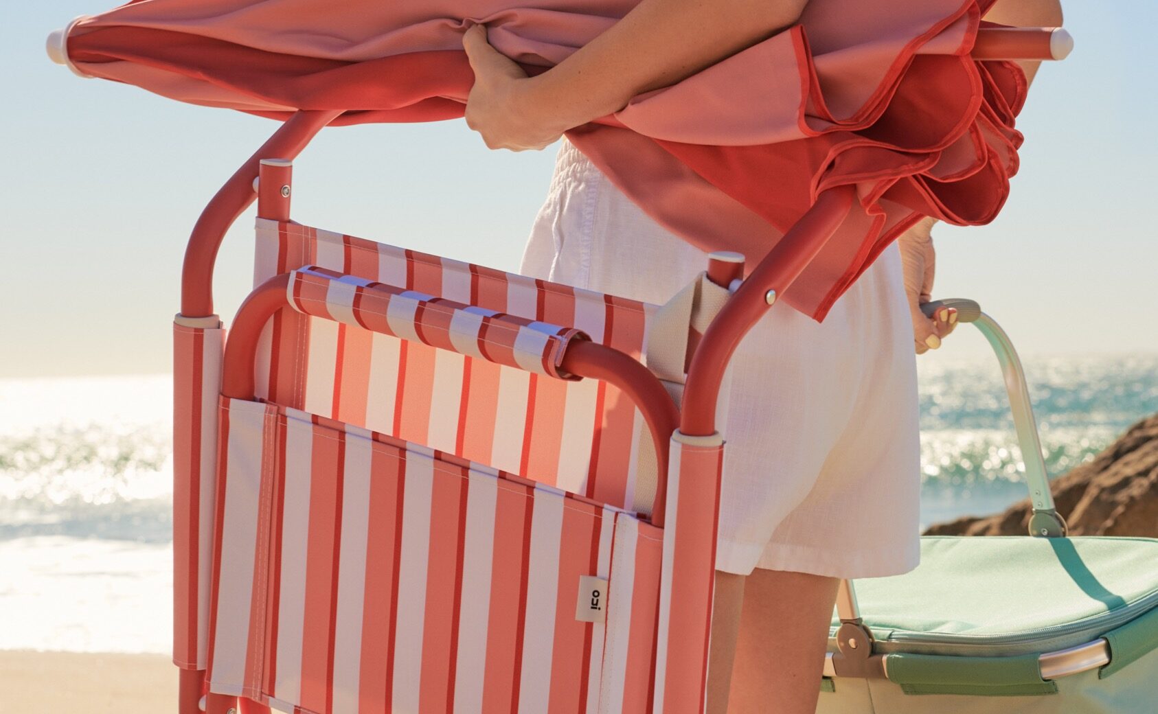 Model carrying OUI beach chair, umbrella and picnic basket.