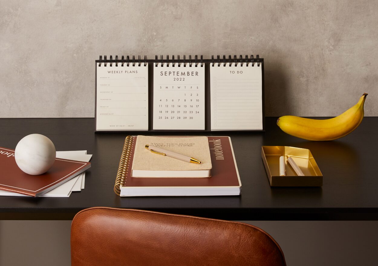 An organized desk with calendar, brass tray and marble paperweight.