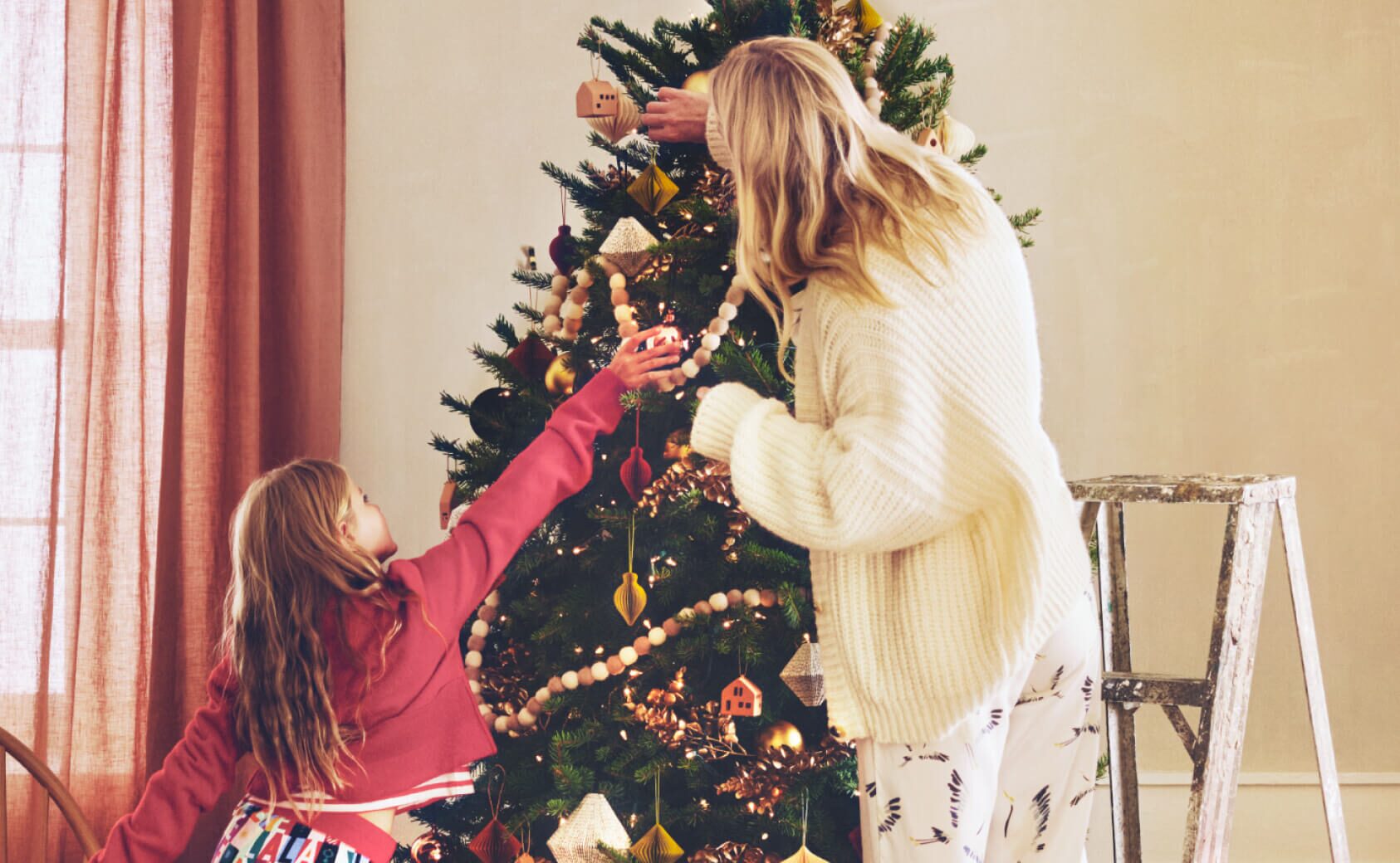 Mother and daughter trimming a Christmas tree.