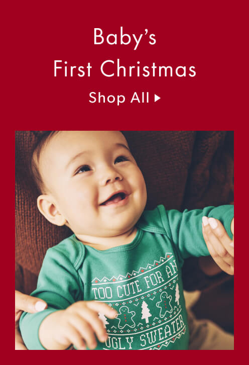 A happy baby wearing a green onesie that says "Too cute for an ugly sweater"