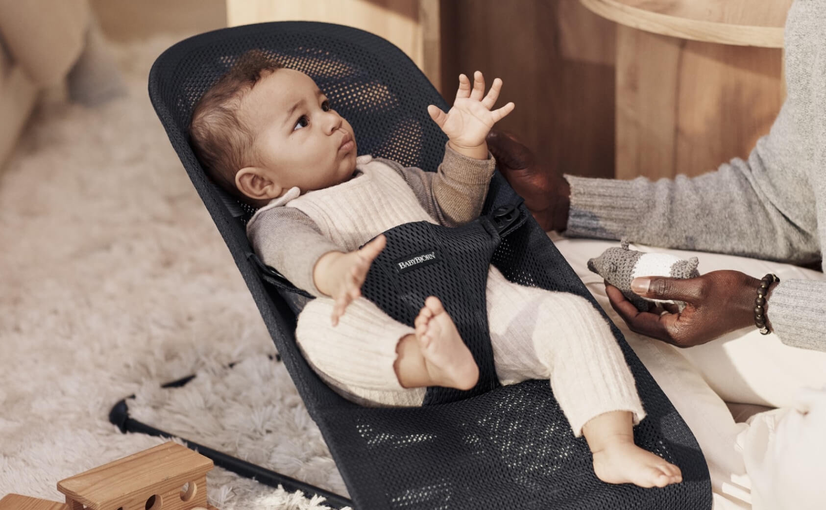 A baby sitting in a black mesh bouncer from BabyBjorn.