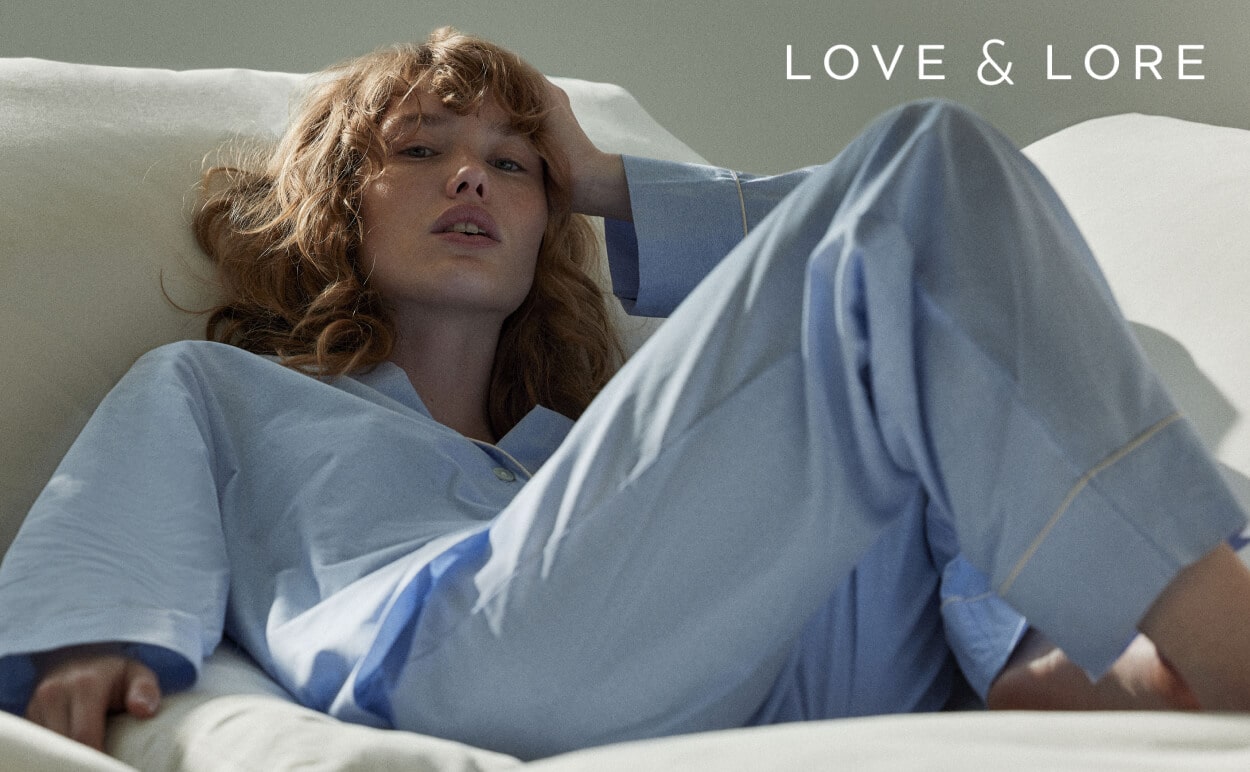 A woman laying on a bed in blue Love & Lore pajamas.