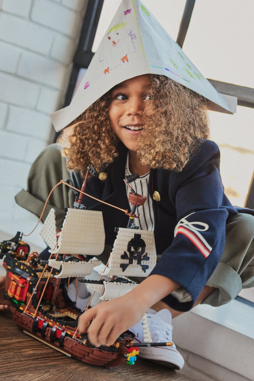 Child wearing a paper hat plays with LEGO pirate ship