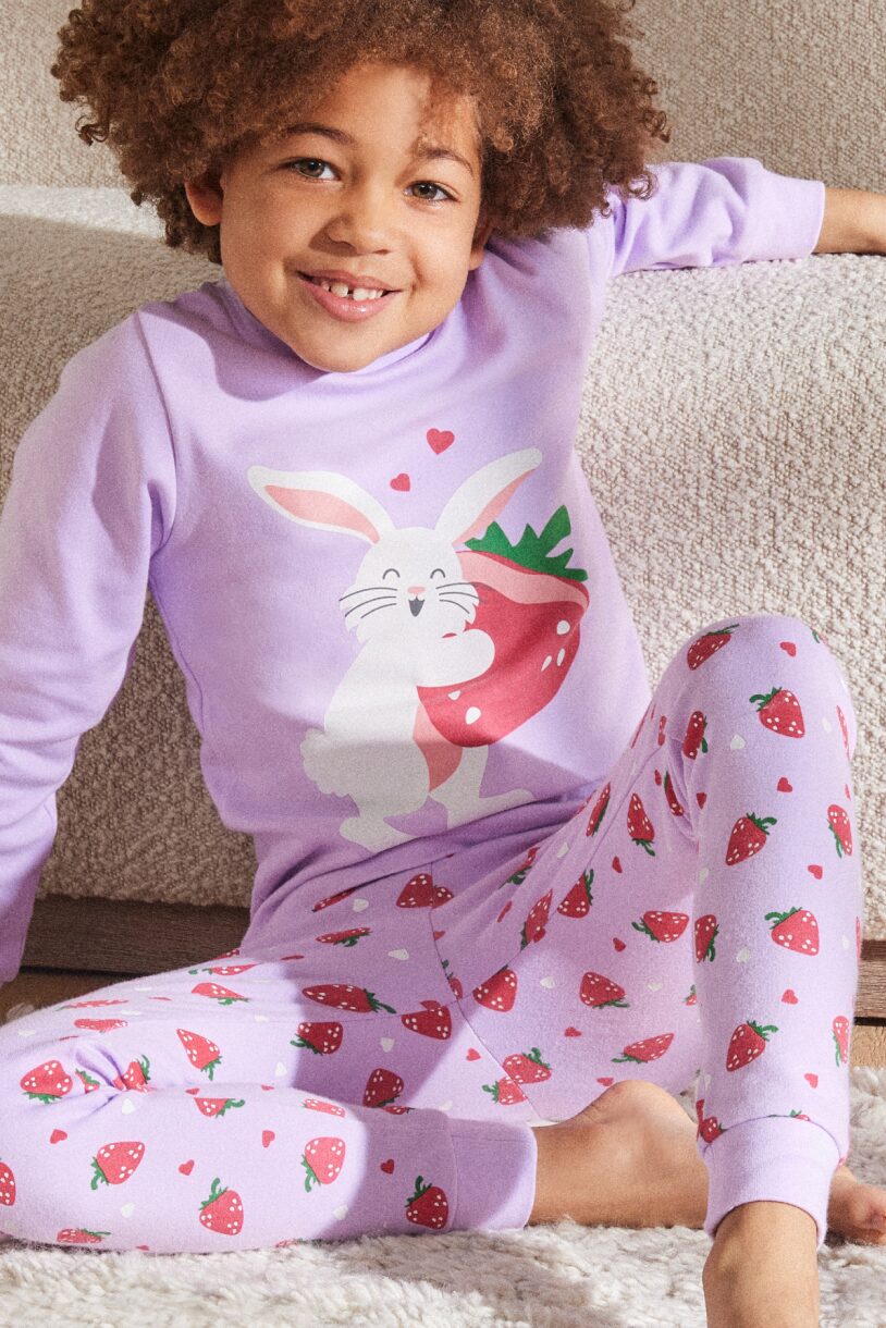A gap-toothed smiling child wearing a purple pajama set with strawberries and a bunny on it.
