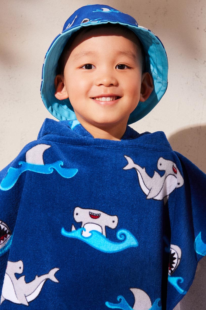 A child wearing a shark print bucket hat and poncho towel.