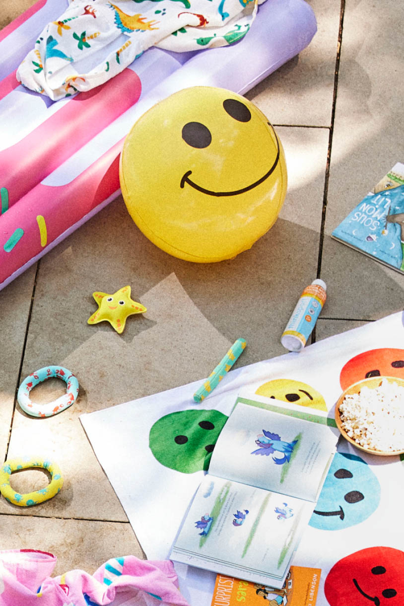 A kids' beach towel, sunscreen, beach ball, and popsicle pool float