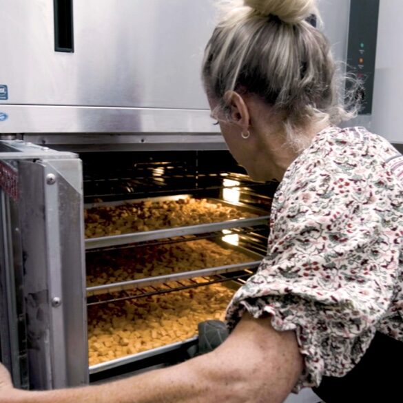 A woman checking on croutons baking in an oven.