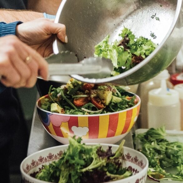 Freshly dressed salad being transferred into a patterned serving bowl.