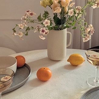 @indigo instagram post: White table topped with Oui organic stoneware, coupe glasses, two oranges, one lemon, and a Oui organic stoneware pitcher filled with flowers.